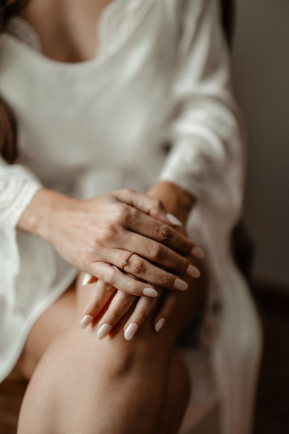 Close-up series of hands gently touching skin in soft natural lighting against white clothing background.