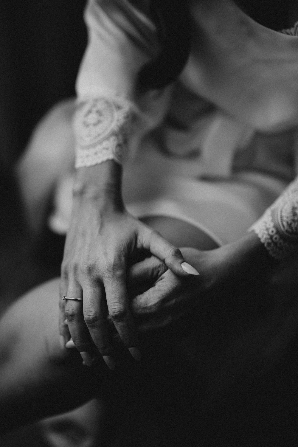 Black and white close-up of hands with delicate lace detail and an engagement ring in an intimate moment.