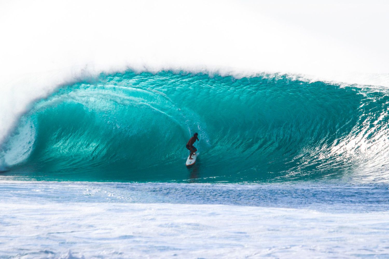 Hawaii surf photography of a surfer riding a massive turquoise barrel wave at Banzai Pipeline.