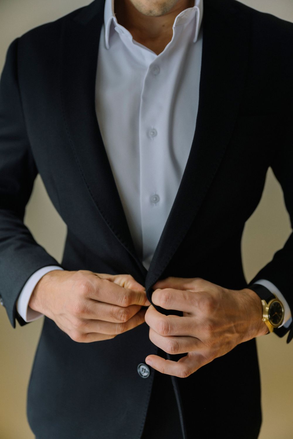 Close-up shots of hands buttoning a formal black suit jacket with a white dress shirt.