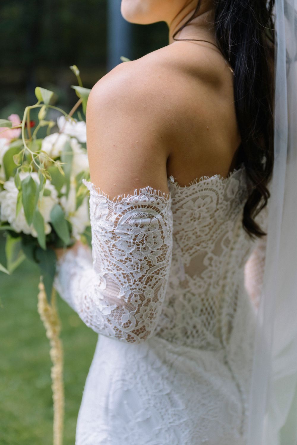 Close-up details of a delicate white lace wedding dress bodice with intricate floral patterns in an outdoor setting.