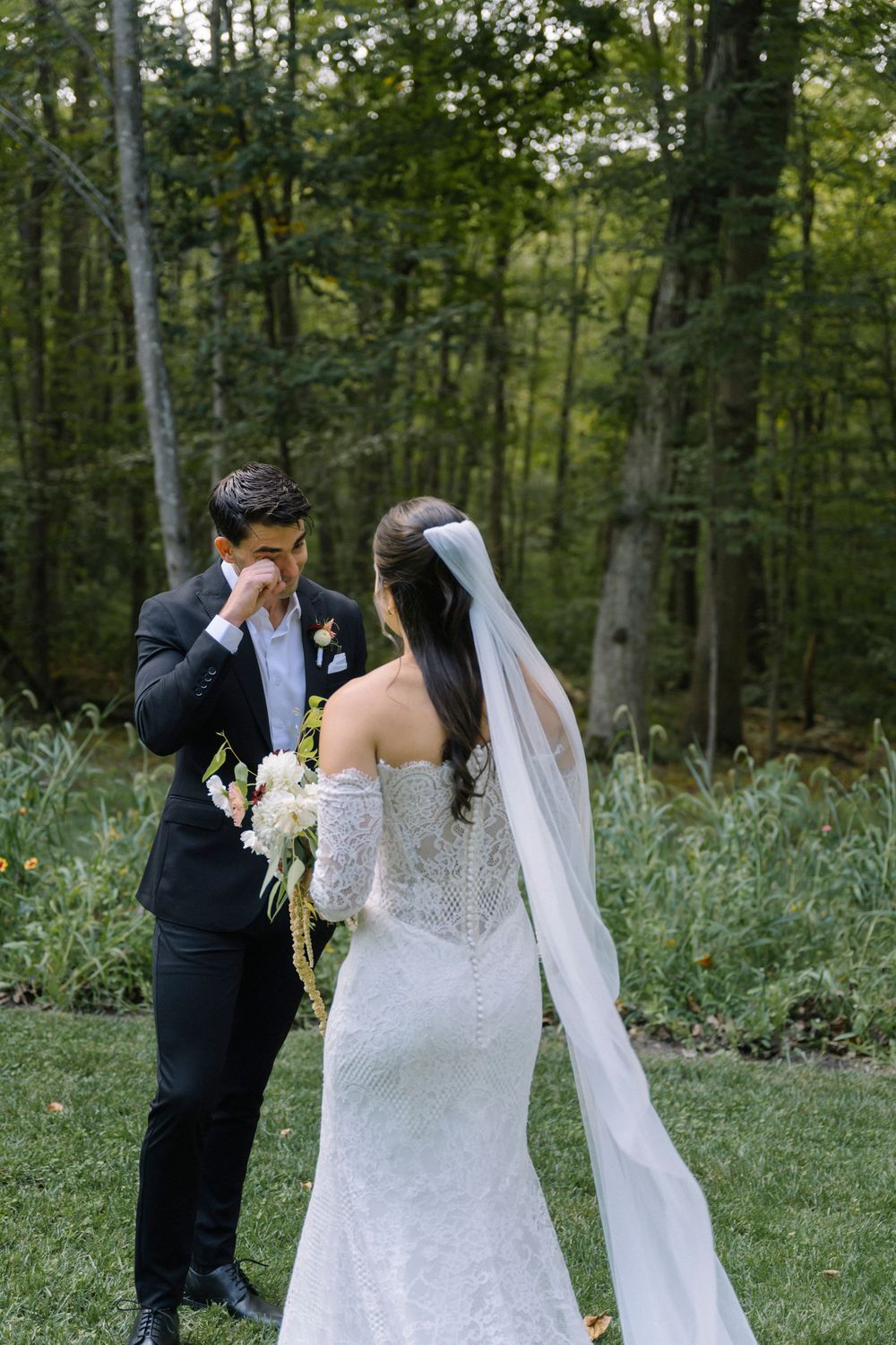 Wedding couple shares intimate moment in forest setting with flowing white veil.