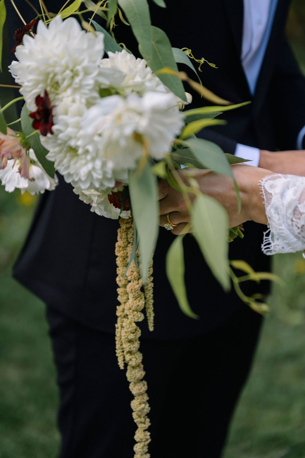 White chrysanthemum flowers and green foliage create an elegant wedding bouquet held against a dark background.