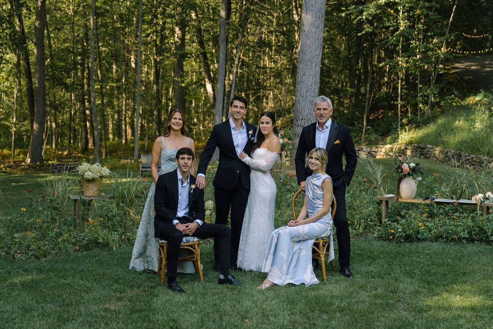Wedding party gathers on grassy lawn surrounded by forest trees.
