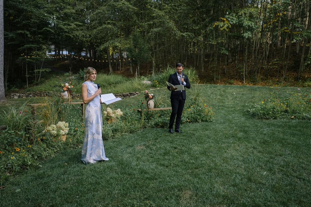 Wedding party gathered in a scenic outdoor forest setting with green grass and tall trees.
