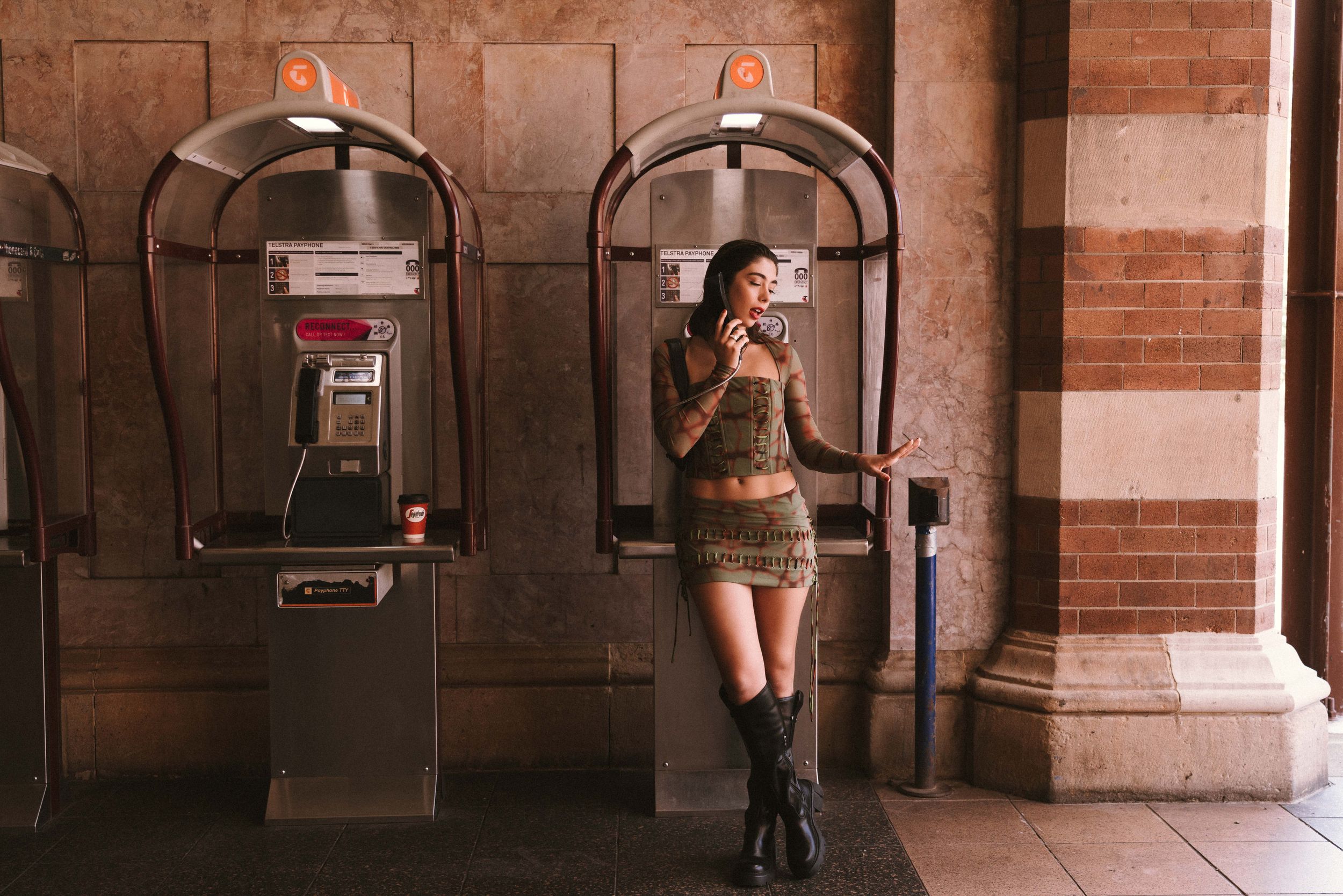 Urban fashion portrait by vintage pay phones in brick archway.