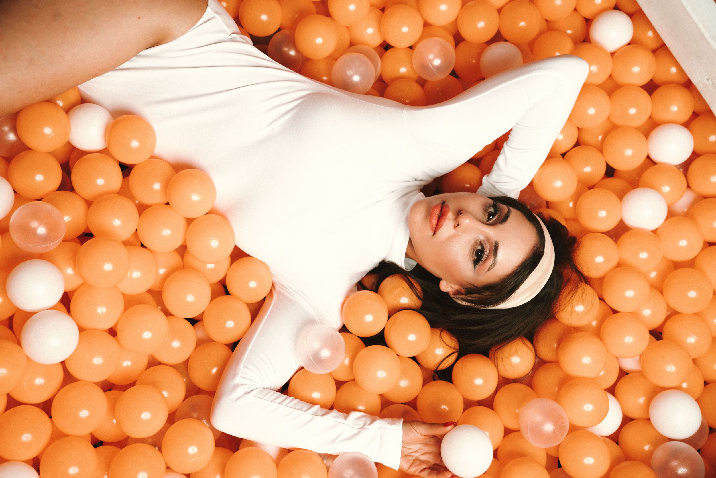 Creative portrait in white outfit laying in orange and white ball pit.