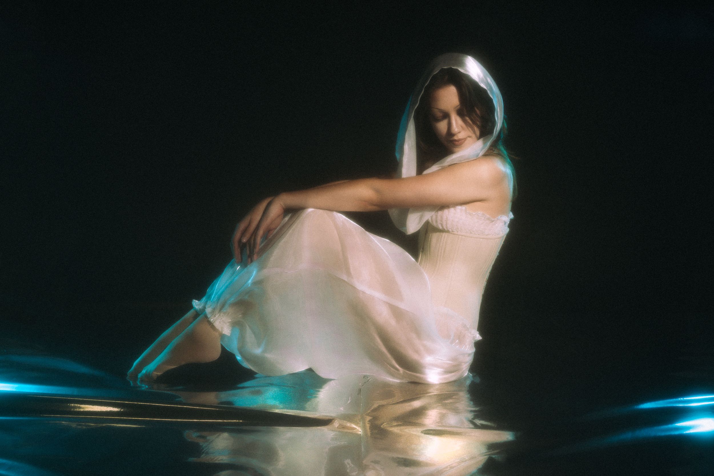 A ballet dancer in a white dress performs a graceful pose against a dark background with blue lighting accents.