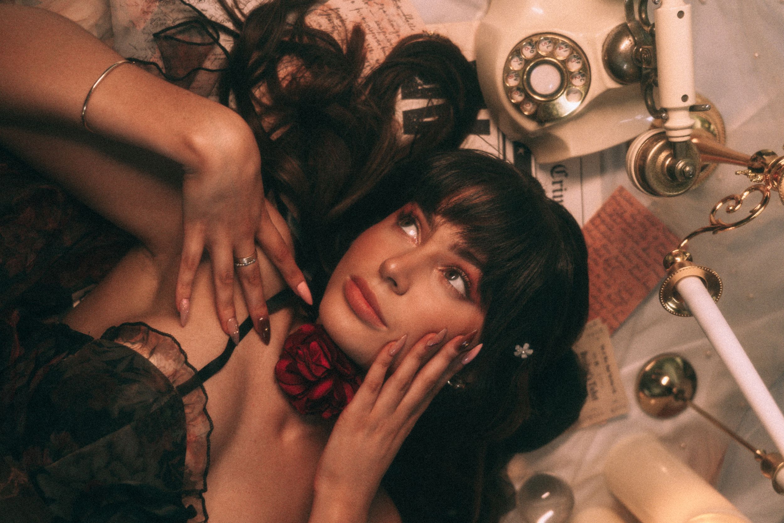 A person lies on the ground with dark hair while surrounded by vintage telephone and mechanical parts in a dreamy setting.