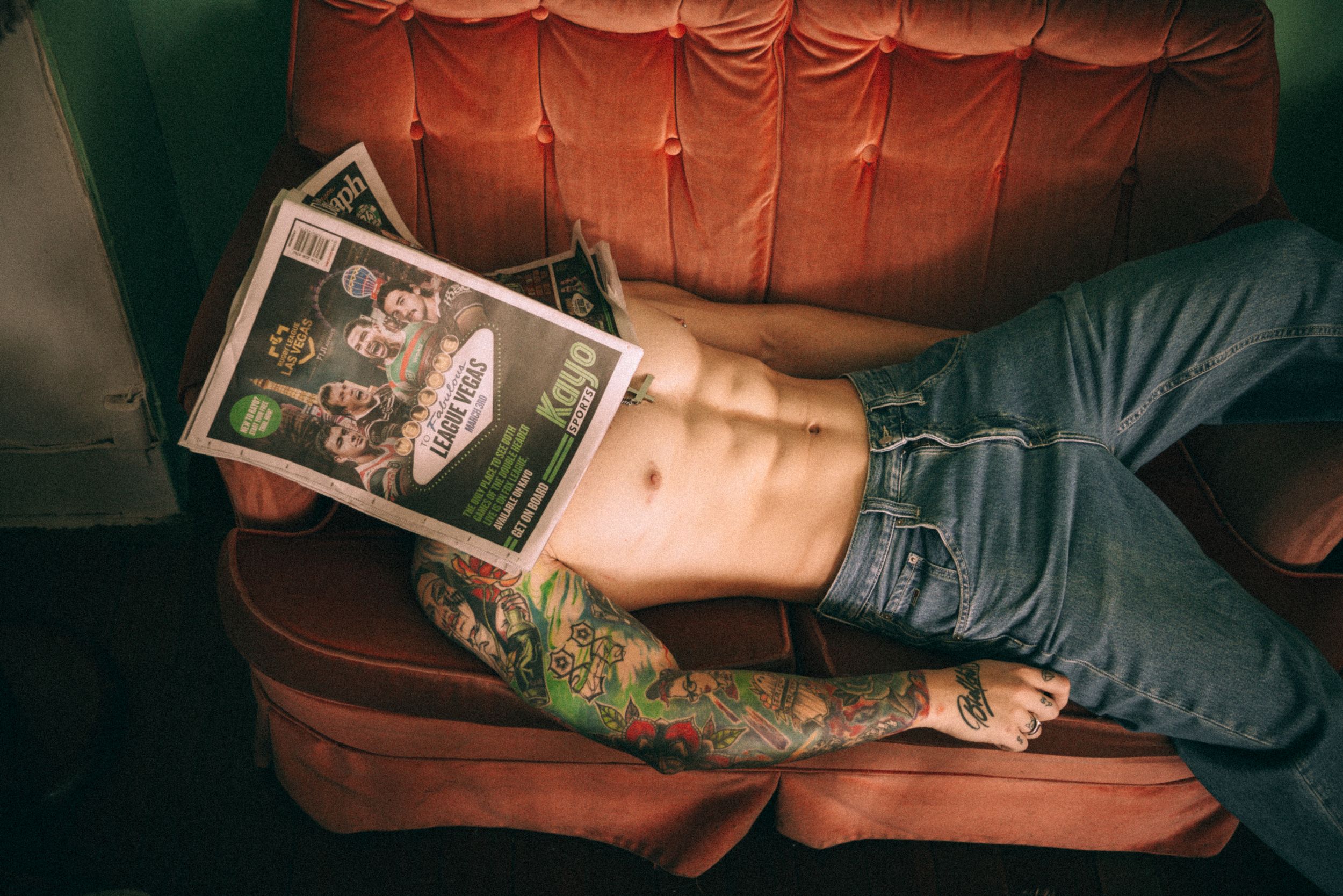 Person lying on orange couch showing tattoo while holding vintage photo.