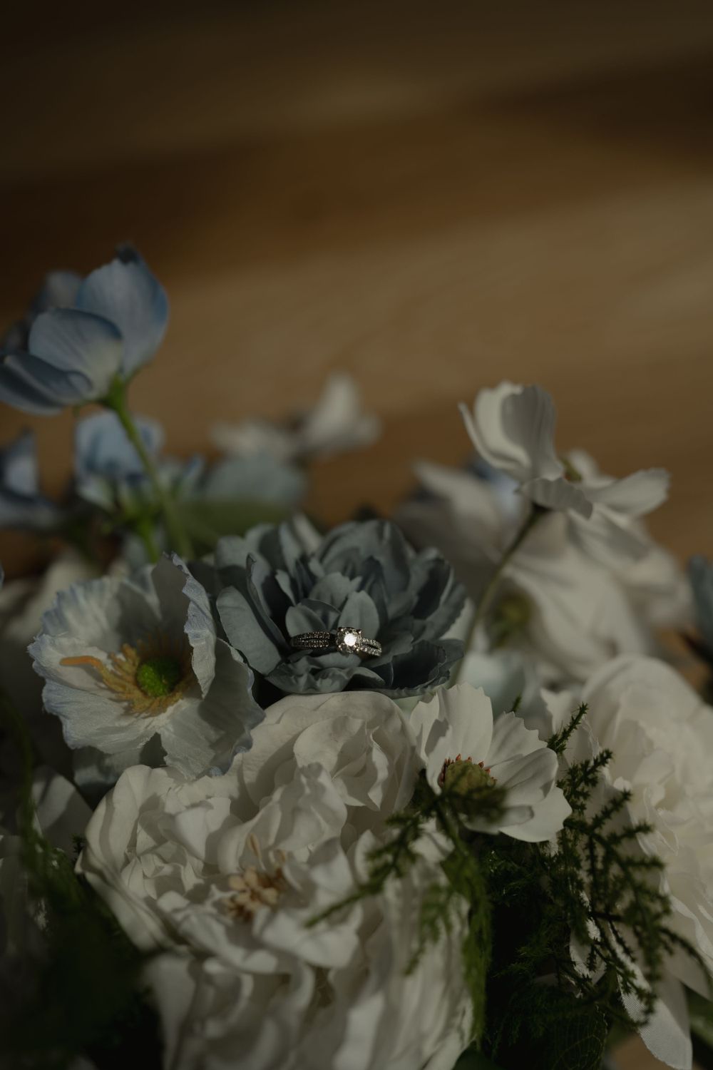 Delicate white flowers with blue accents in a moody dark setting on wooden surface.