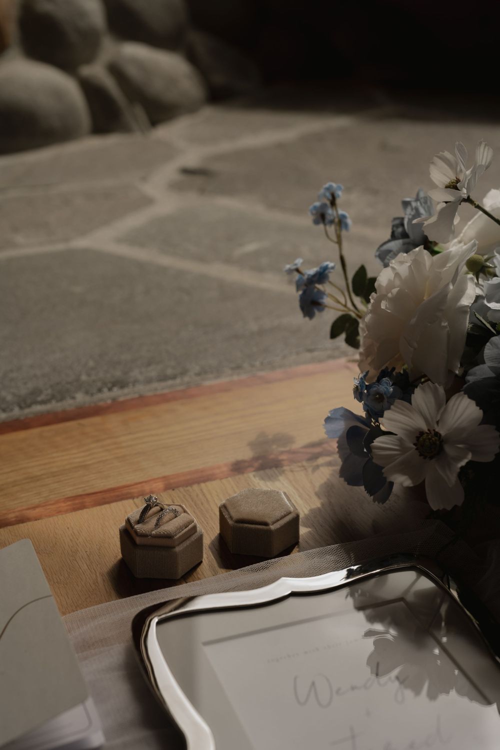 Wedding details with hexagonal ring boxes and delicate blue flowers on wooden surface.