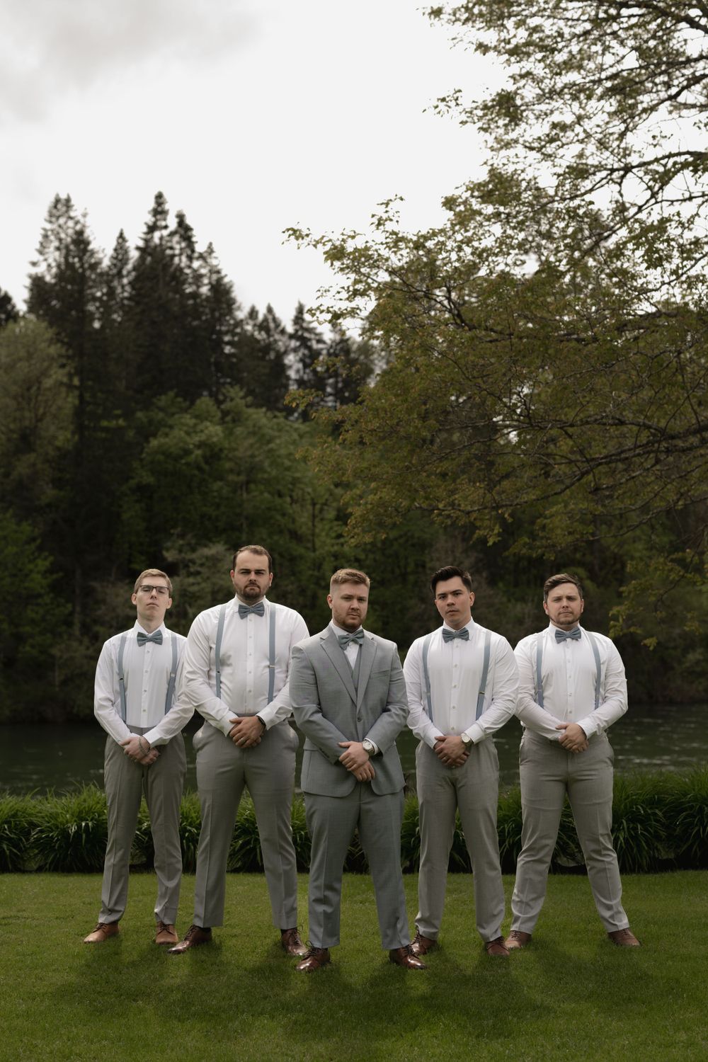 Wedding party in coordinated gray and white attire posed on manicured lawn.