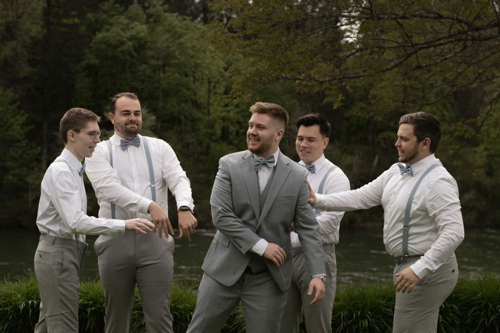 Groomsmen sharing a lighthearted moment outdoors in formal attire.