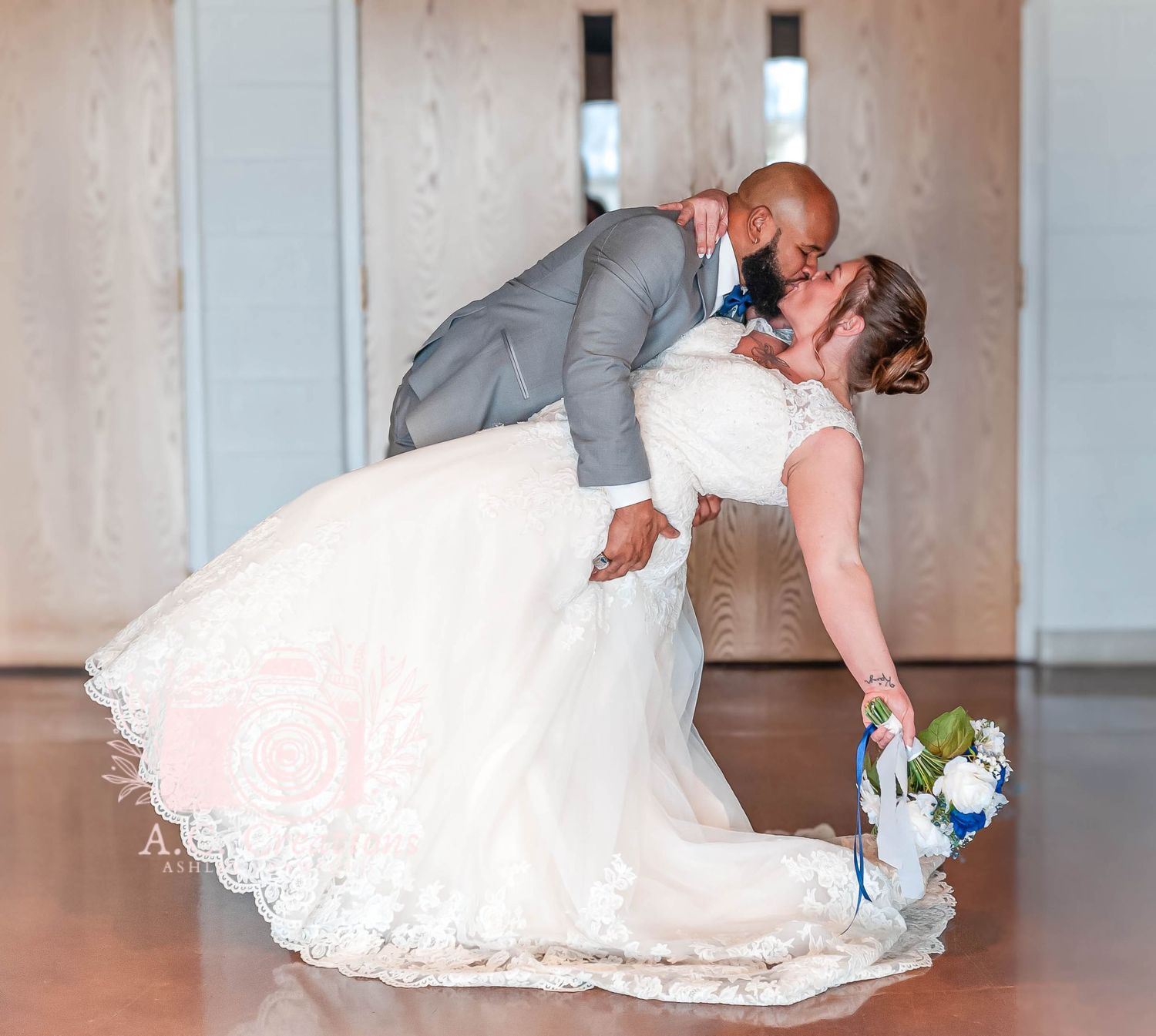 A romantic dip pose between newlyweds, with the bride holding a blue and white bouquet.