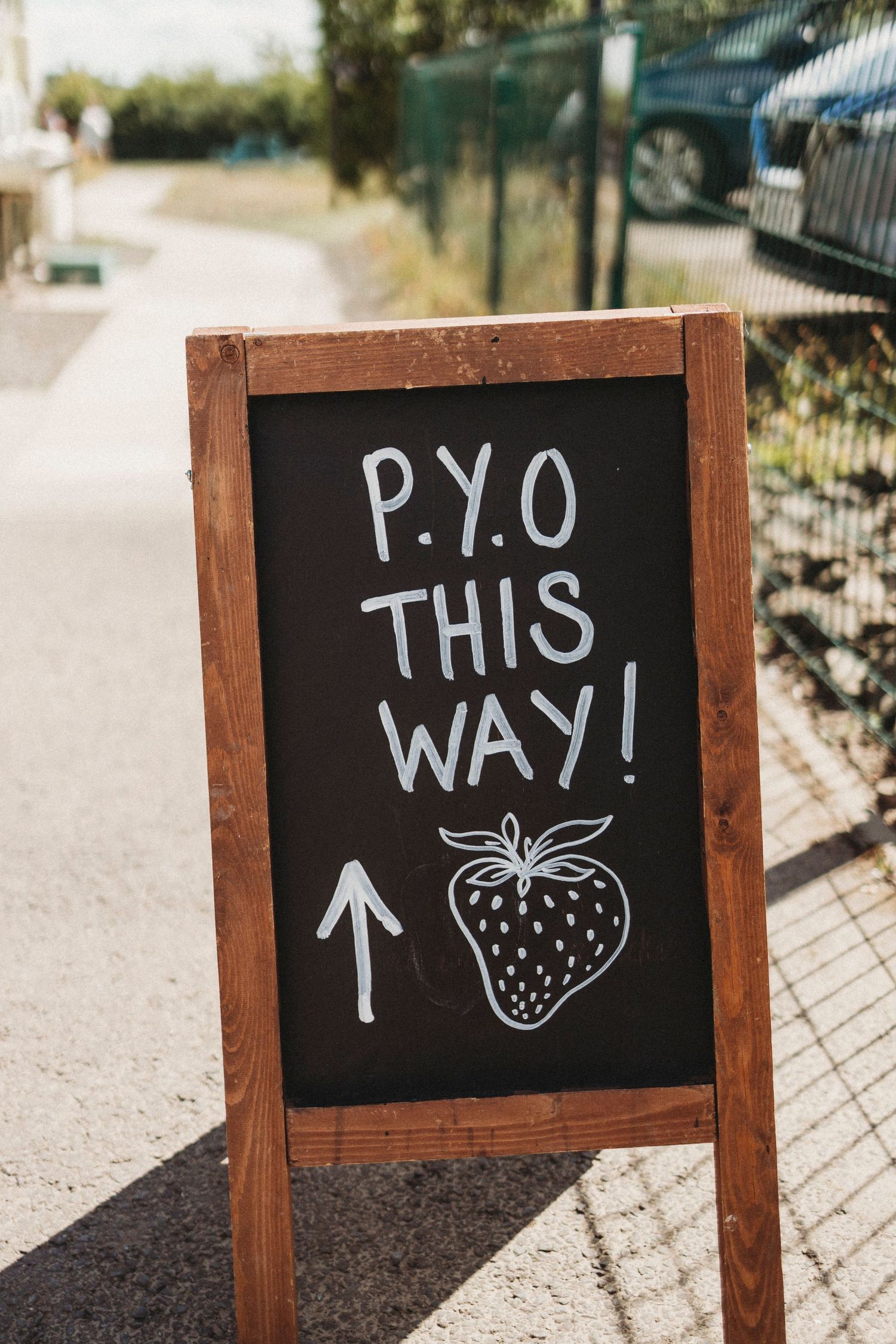 Wooden chalkboard sign with arrow pointing to PYO (Pick Your Own) strawberry field.