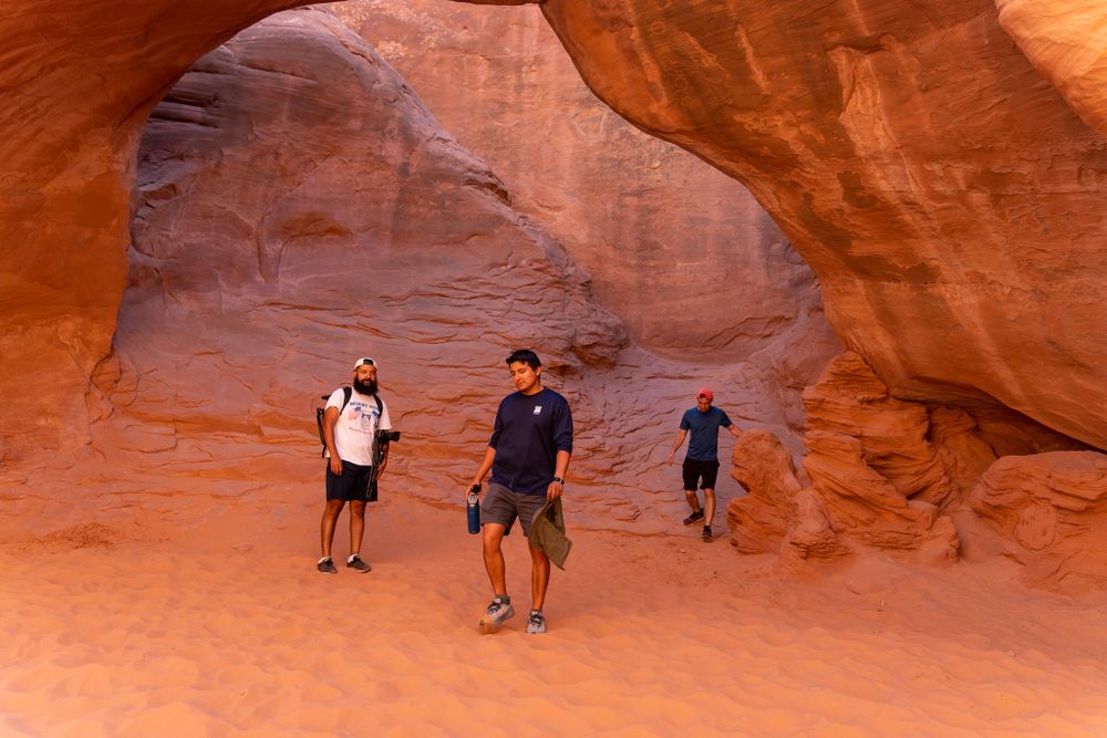 Visitors explore a large natural rock arch formation in the desert.