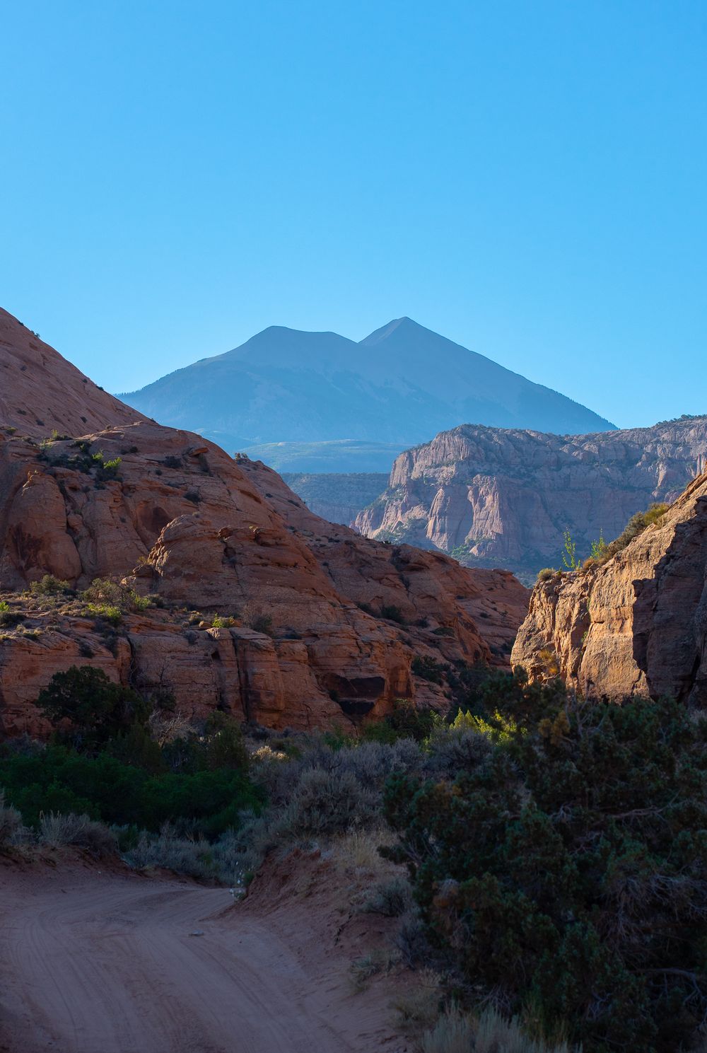 Mountain peaks rise above red rock formations along a desert trail at dusk.