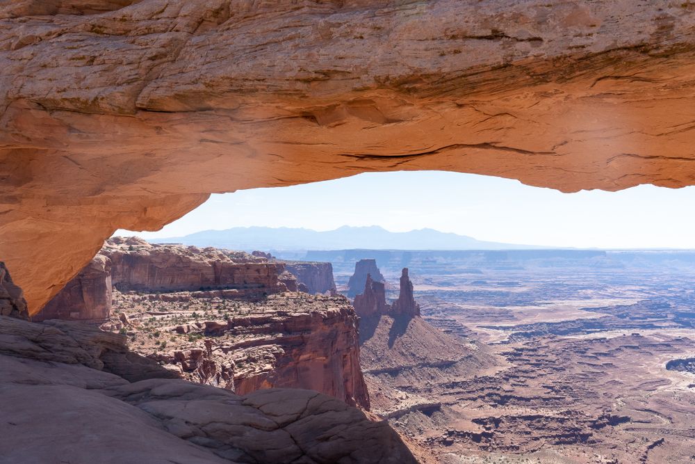 Mesa Arch frames a stunning desert canyon vista with towering rock formations in the distance.