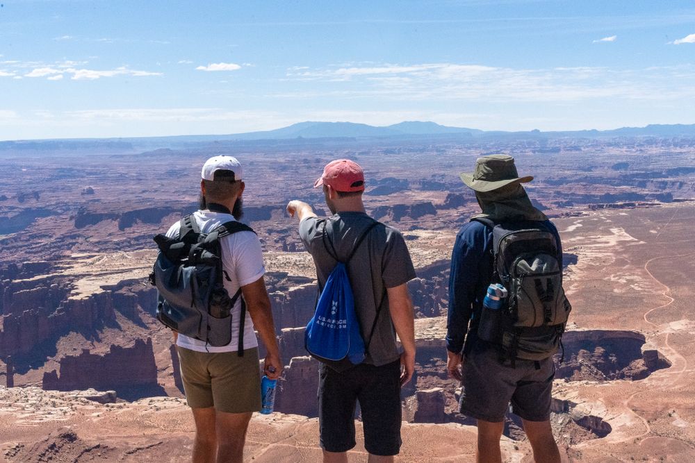 Three hikers admire the vast desert canyon landscape from a scenic overlook point.