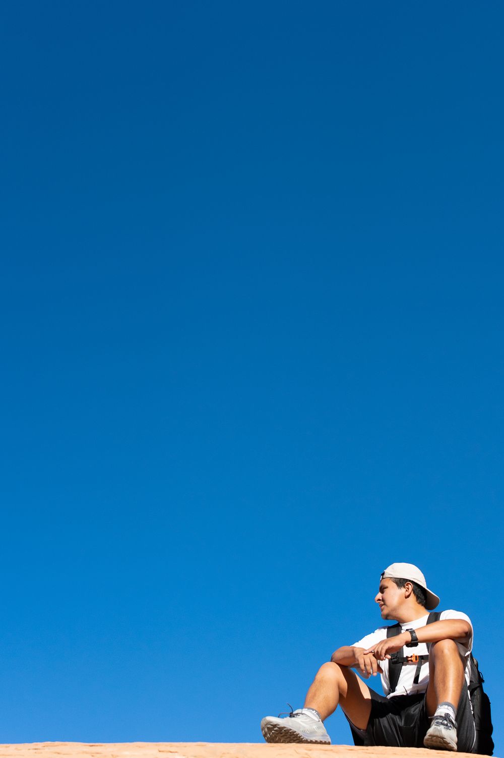 Person resting on red rock overlook against vibrant blue sky while taking a break from hiking.