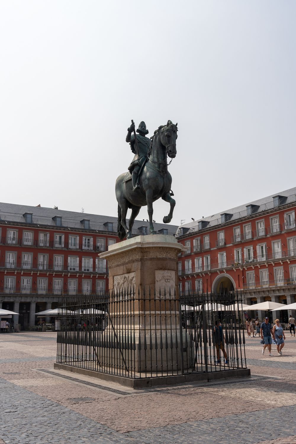Historic equestrian statue in Plaza Mayor Madrid with traditional red buildings.