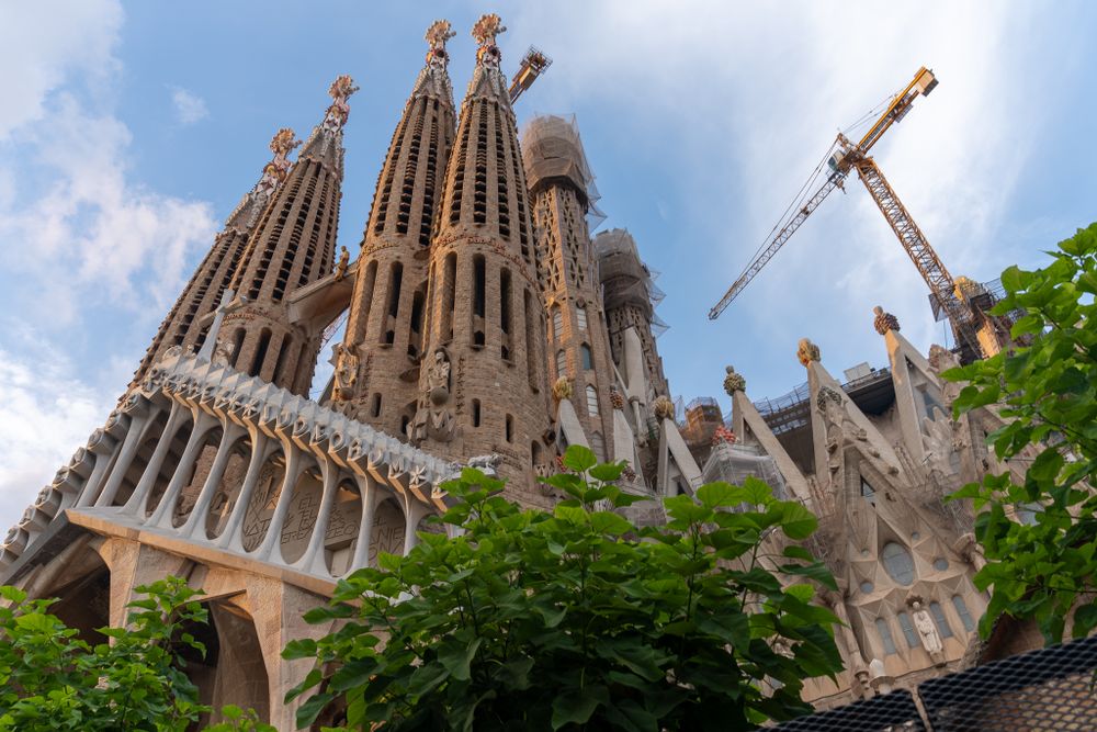 La Sagrada Familia's iconic spires and construction cranes rise against blue Barcelona sky.