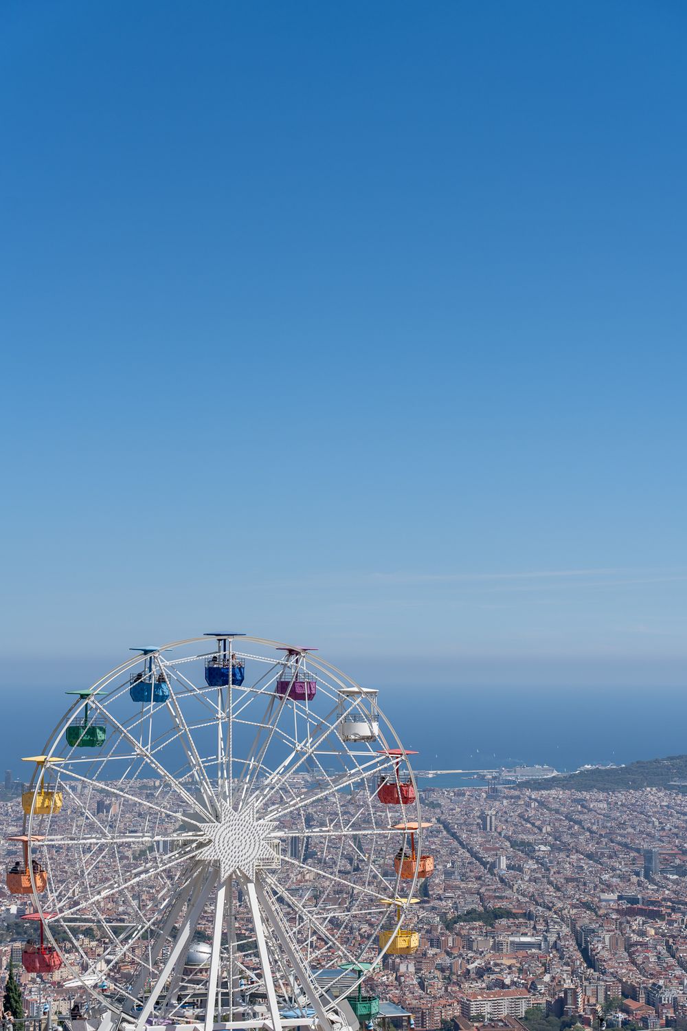Colorful Ferris wheel overlooking Barcelona city skyline against clear blue sky.