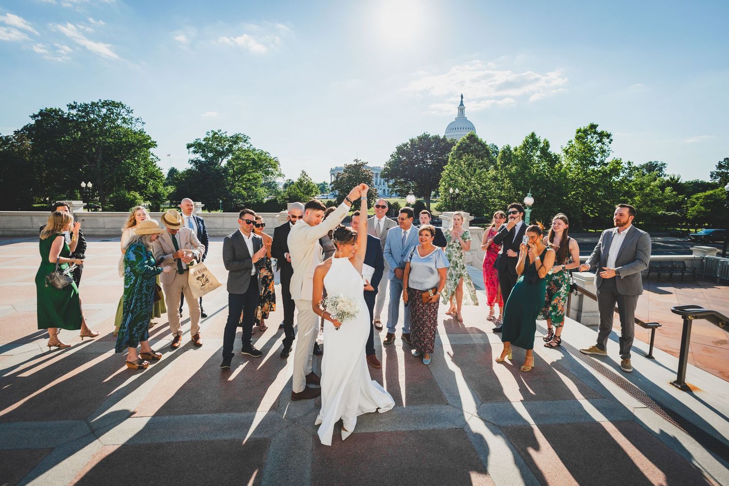 Wedding party poses with dramatic shadows on steps with Capitol dome visible in background.