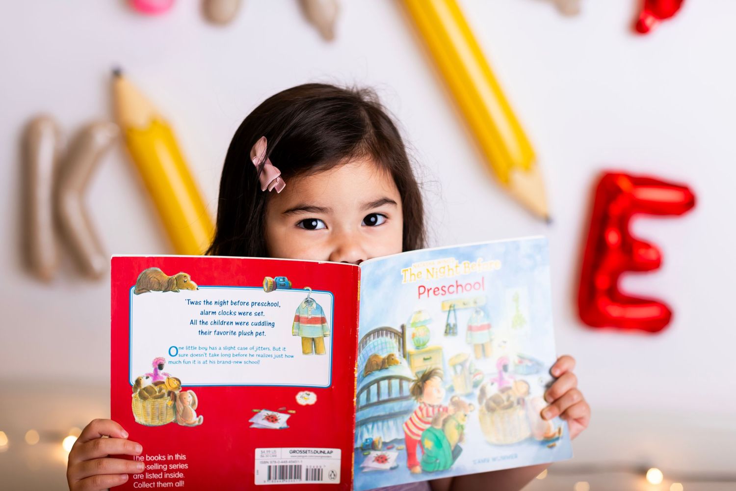 Young student reading educational book against wall with alphabet decorations.