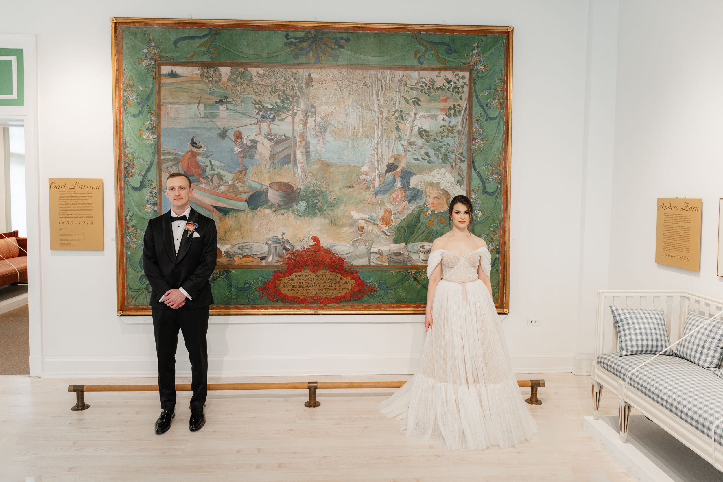 Bride and groom standing apart in a museum gallery before a large ornate painting.