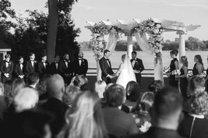 Wedding ceremony guests seated in rows under a white tent canopy with water views.