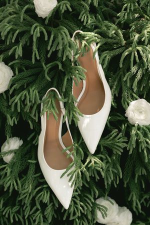 White bridal shoes displayed against fresh green foliage background.