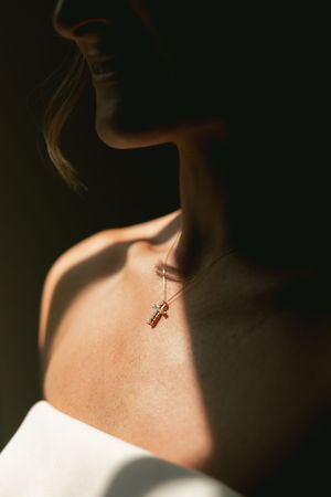 Delicate gold cross necklace pendant captured in dramatic lighting.
