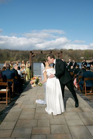 Bride and groom share a first kiss at outdoor lakeside wedding ceremony on a sunny day.