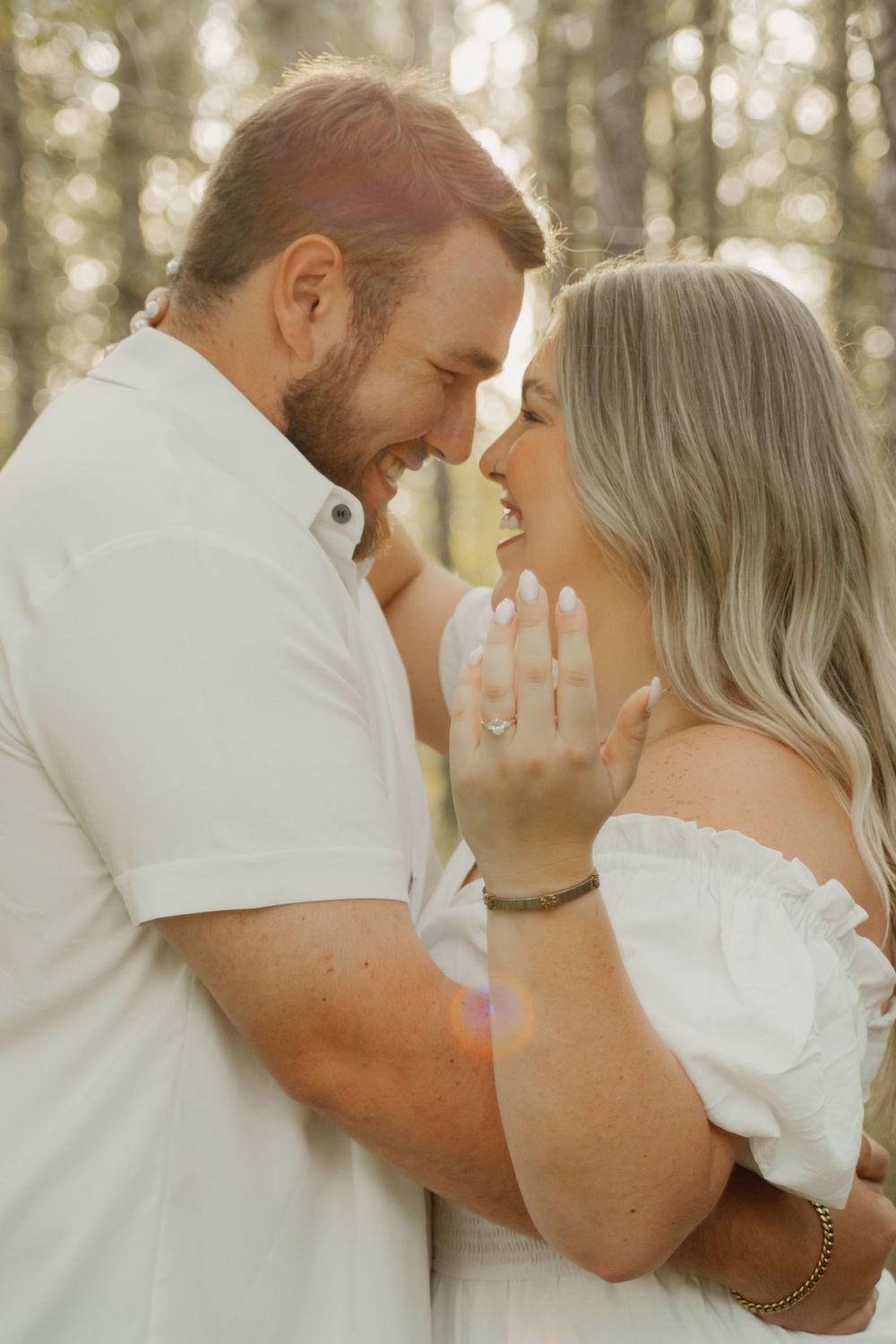 A romantic outdoor photoshoot shows a couple in white sharing intimate moments in a sun-dappled forest setting.