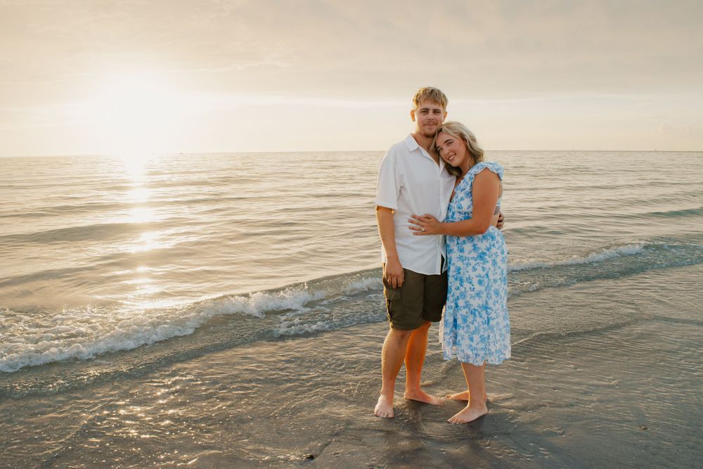 Couple embracing on a sandy beach at golden sunset, waves gently rolling in behind them.