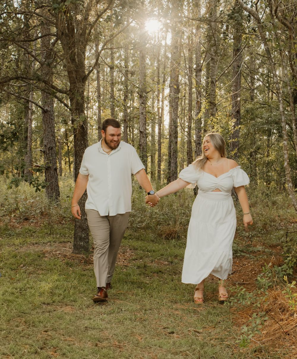 A couple walks and dances together through a sunlit forest setting in romantic wedding attire.