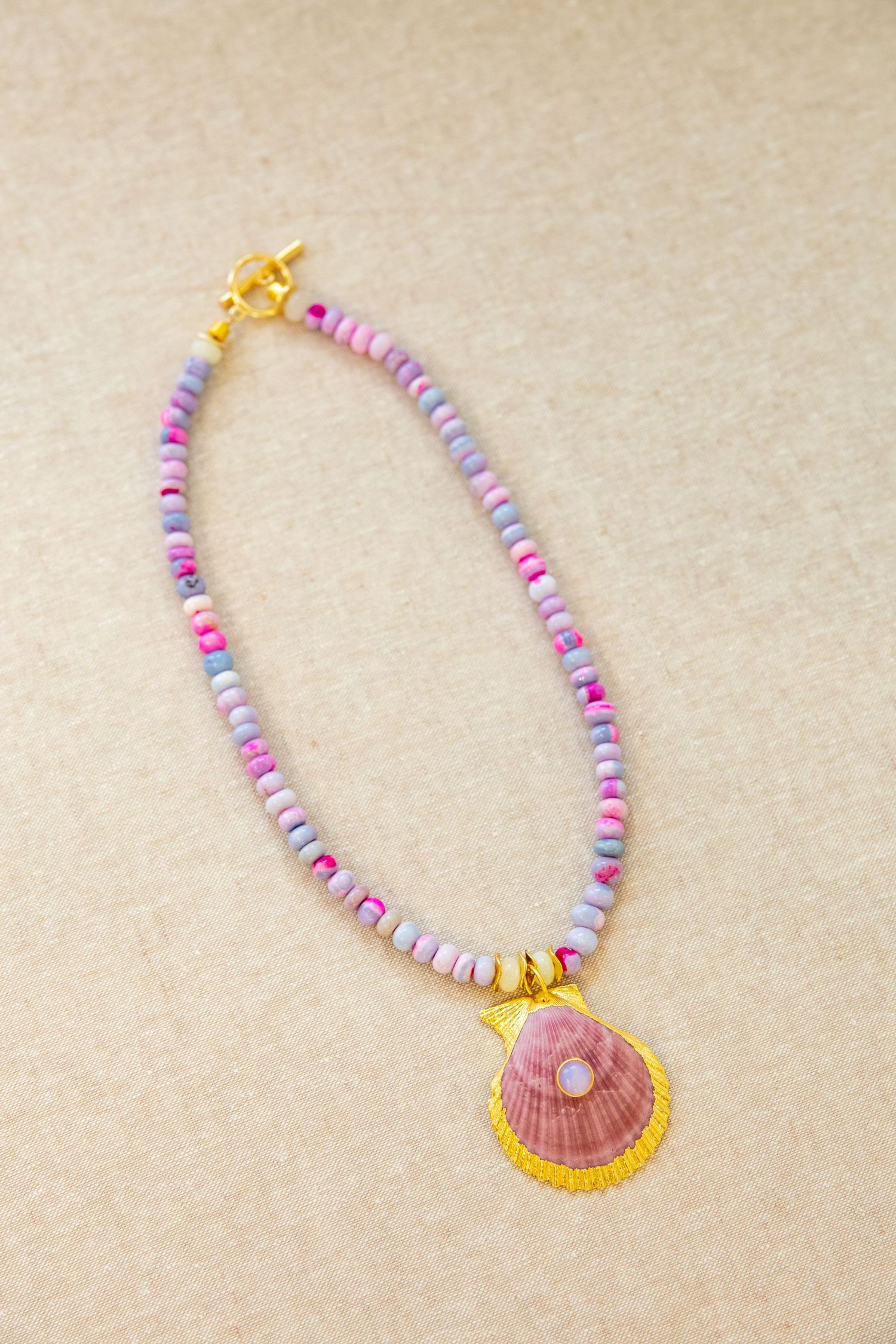 Pastel beaded necklace with pink and purple tones featuring golden-trimmed seashell pendant.