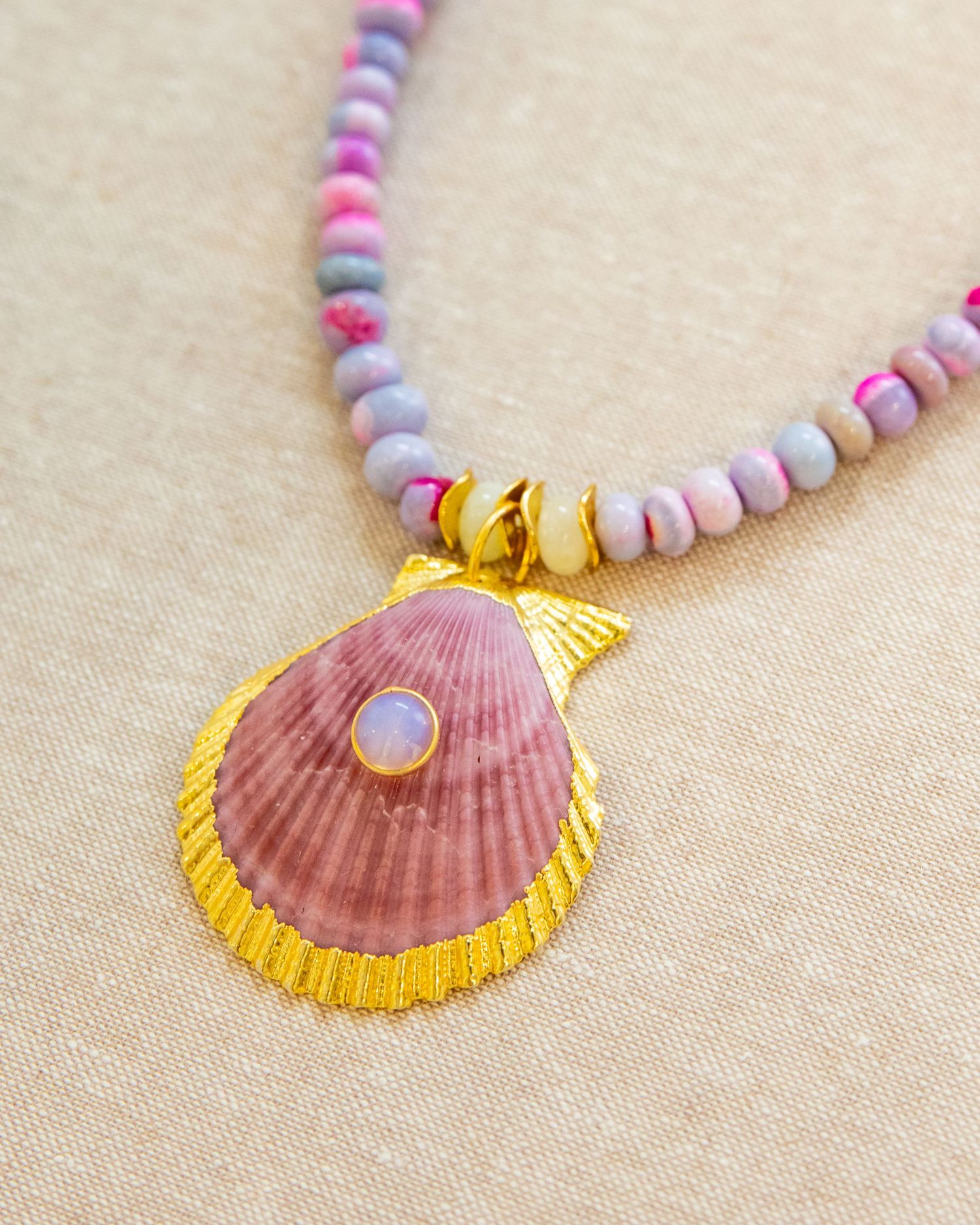 Close-up detail of pink seashell pendant necklace with gold trim and lavender beaded chain.