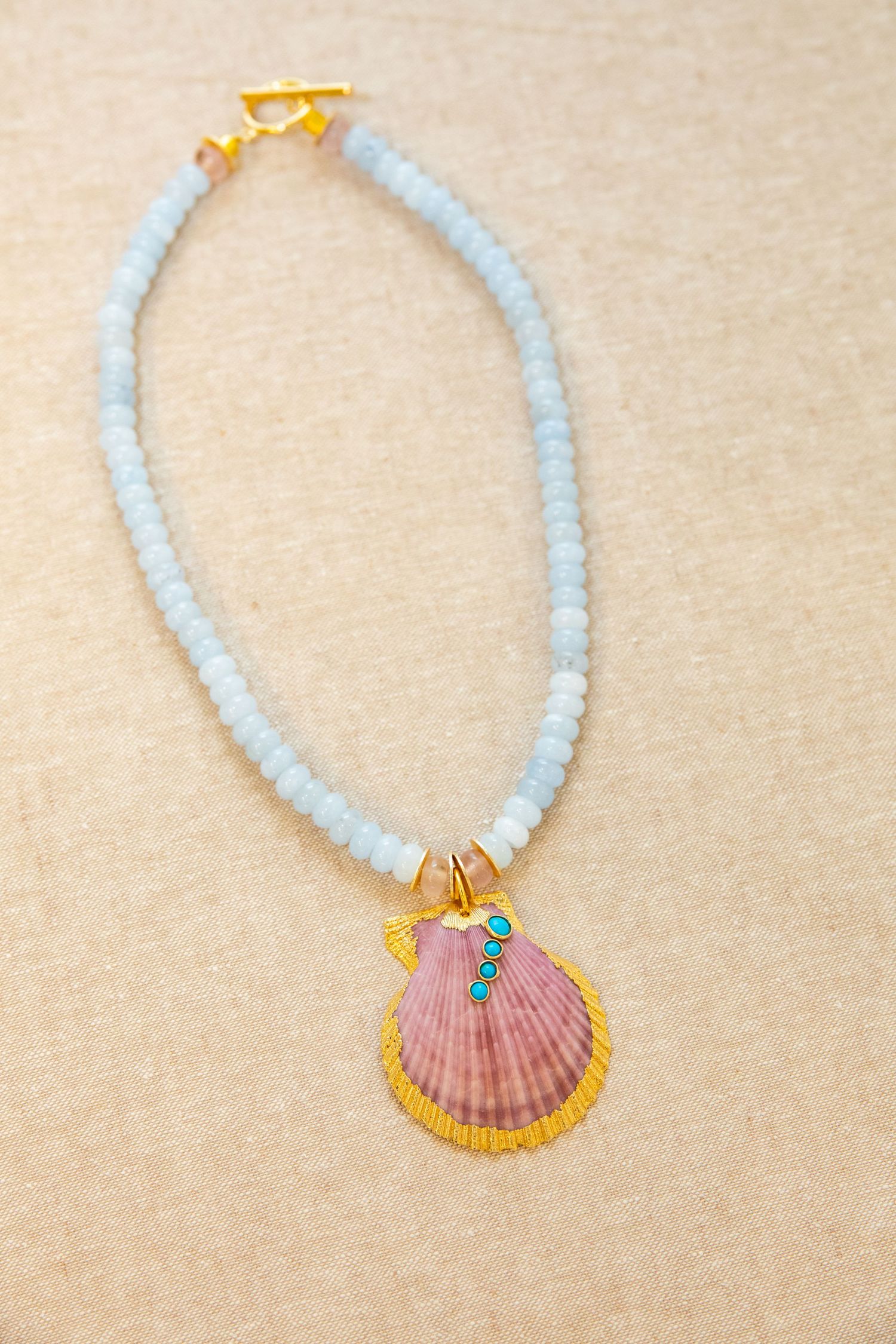 Handmade beaded necklace featuring a pink seashell pendant with gold trim and light blue beads.