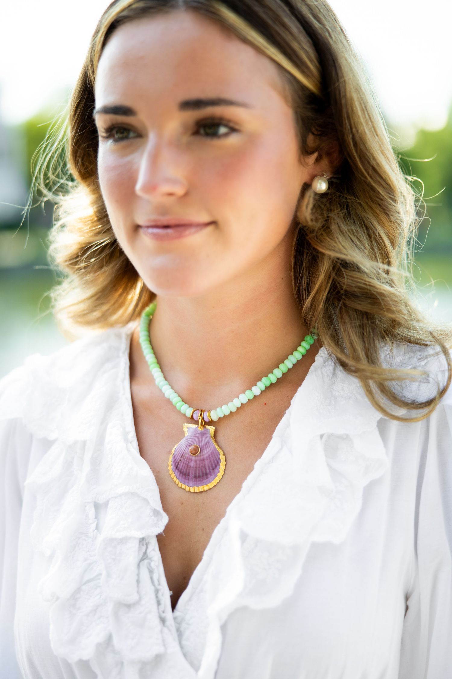 Close-up view of a white ruffled blouse paired with a mint green beaded necklace and purple shell pendant.
