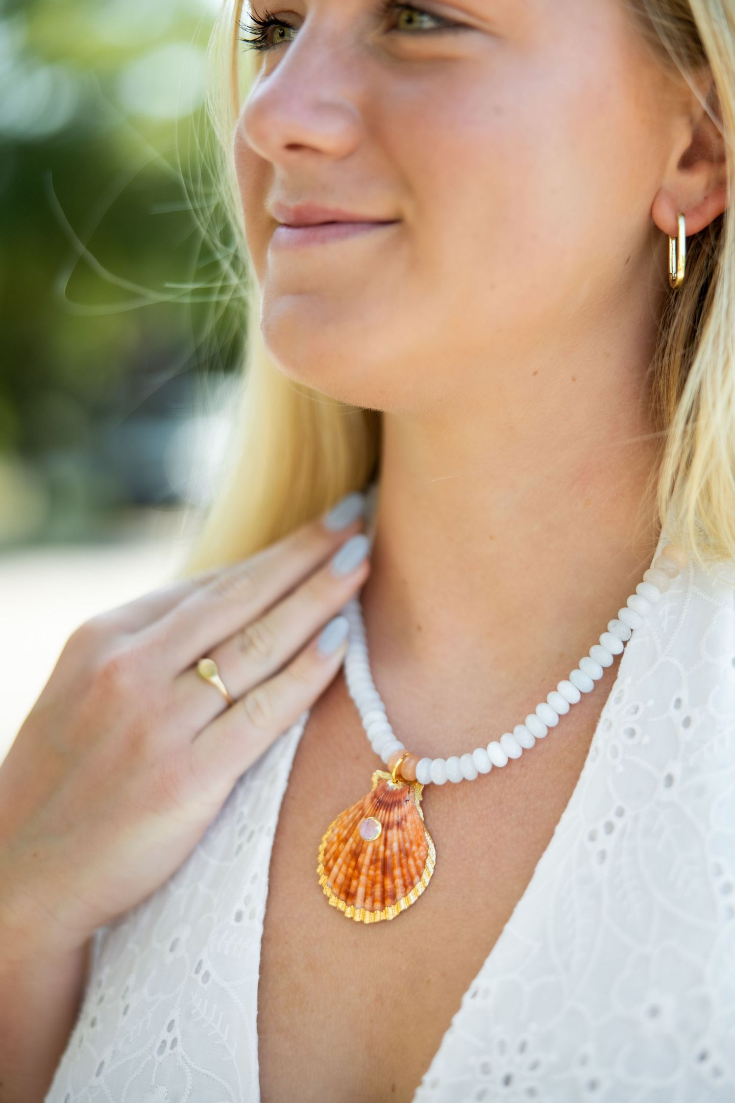 Close-up of a seashell necklace with white beads worn with a white dress in natural lighting.