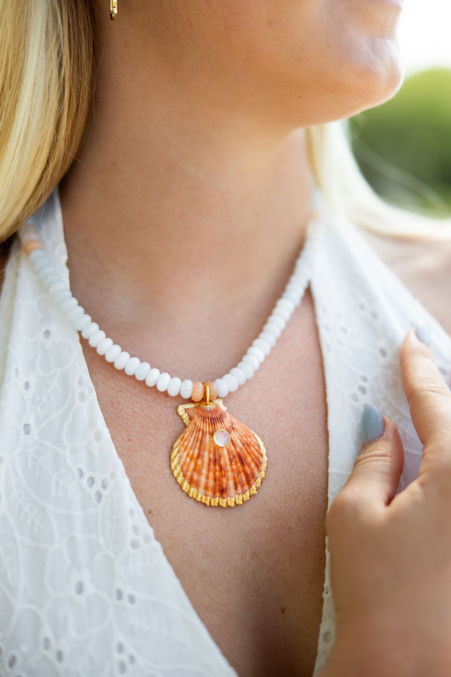 Close-up shots of a delicate white beaded necklace with an orange seashell pendant against white lace fabric.