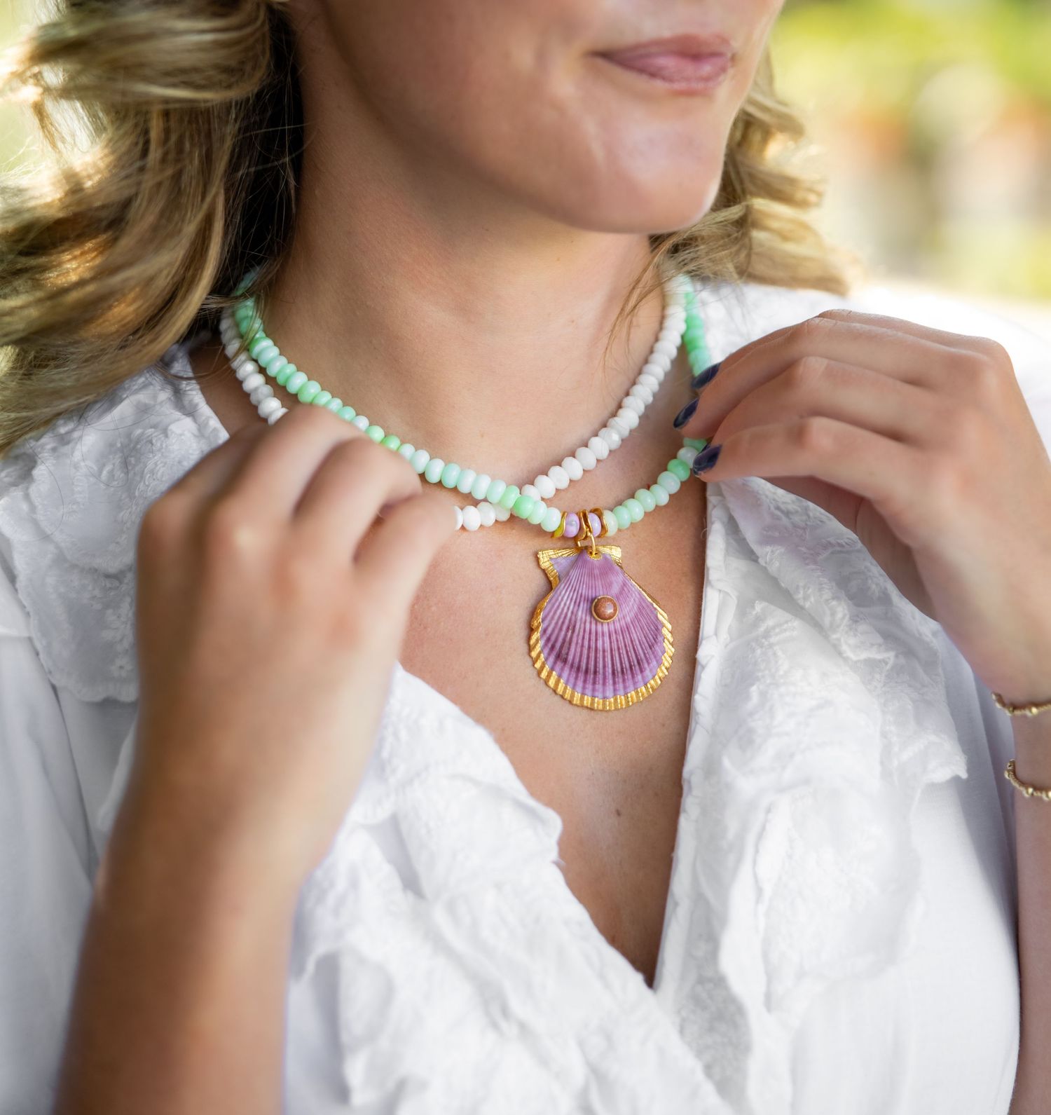 Close-up view of a colorful beaded necklace with a pink shell pendant against a white blouse.