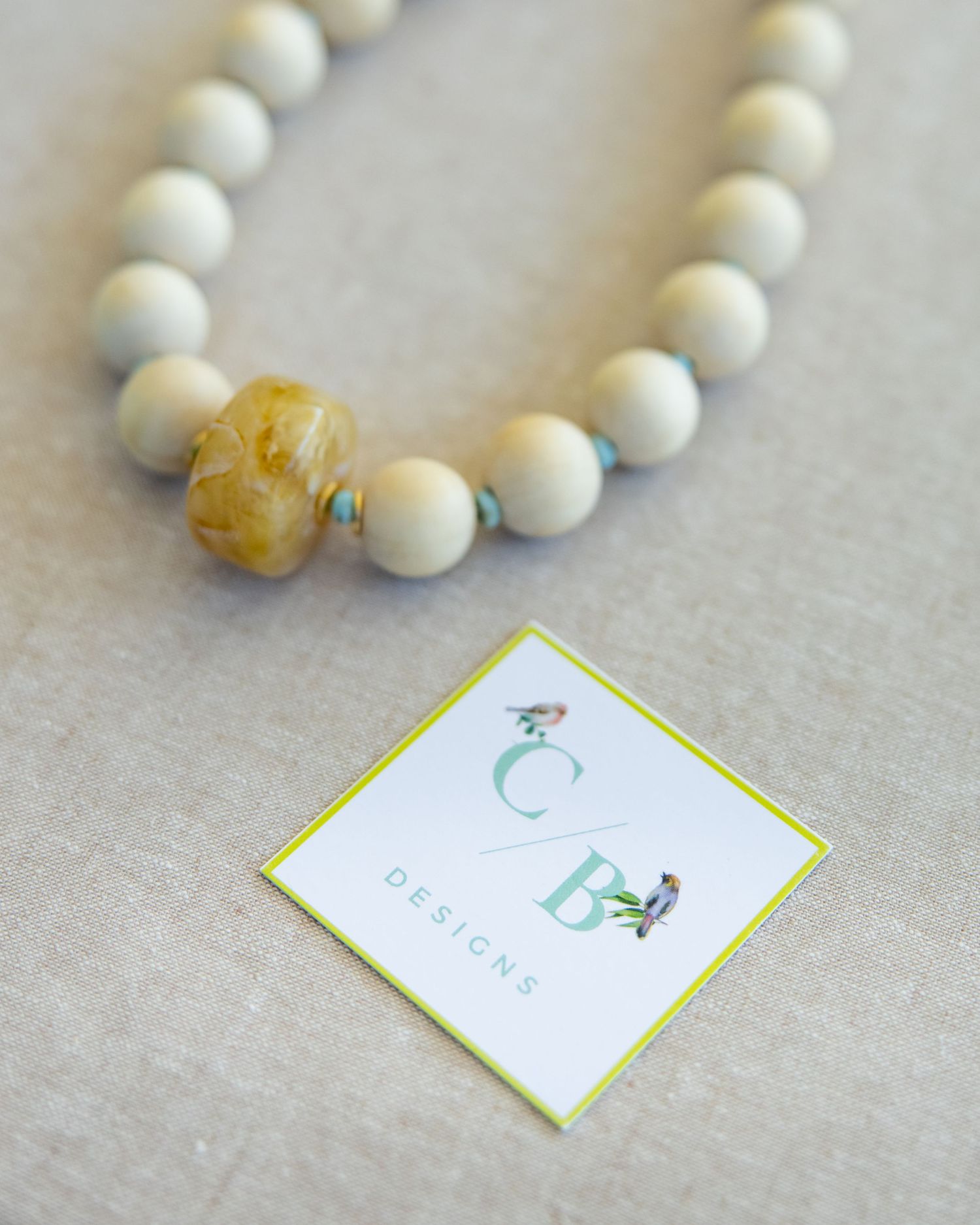 White beaded necklace with business cards showing brand details laid out on light gray surface.