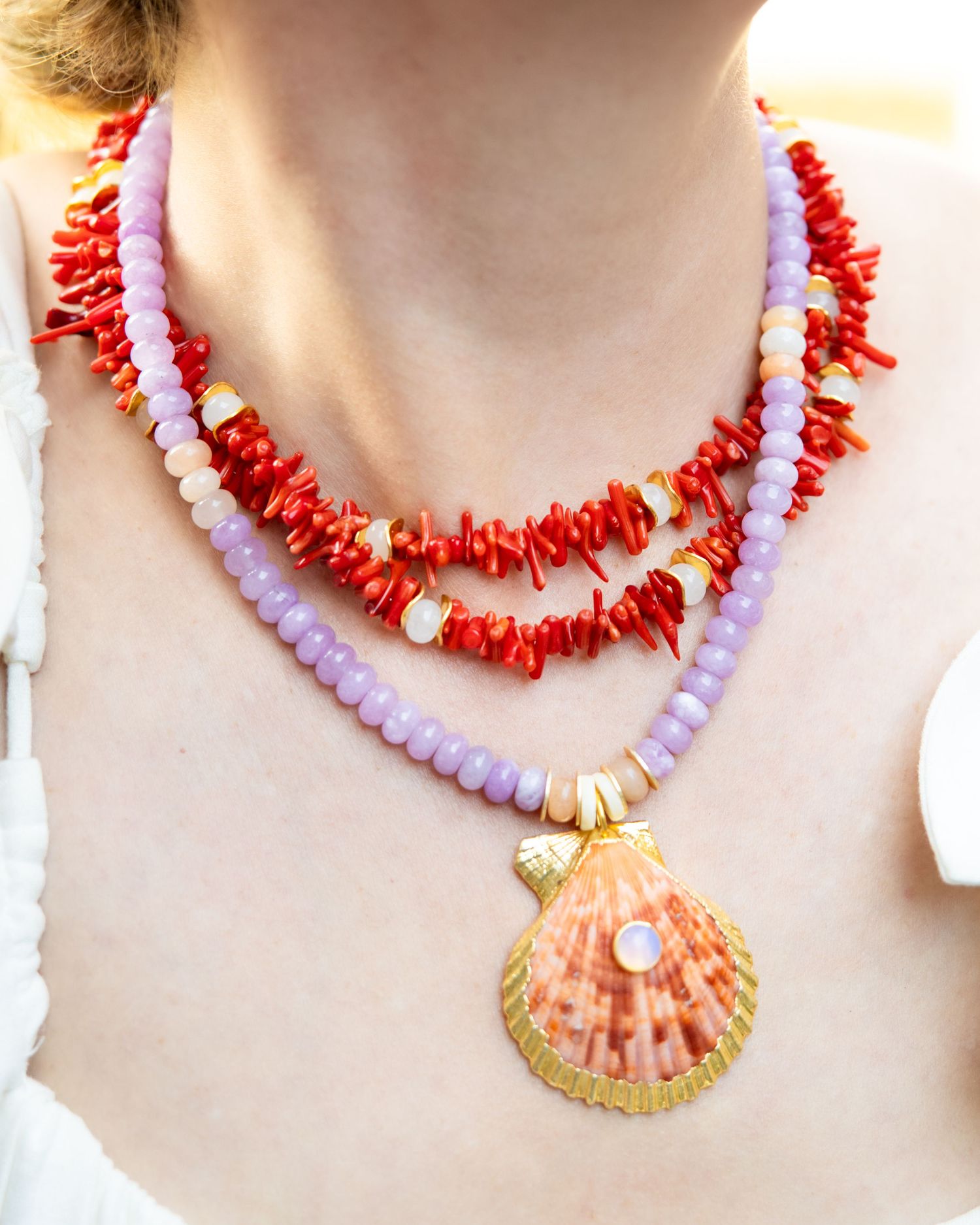 Collection of coral and pearl beaded necklaces with seashell pendants displayed on a light background.