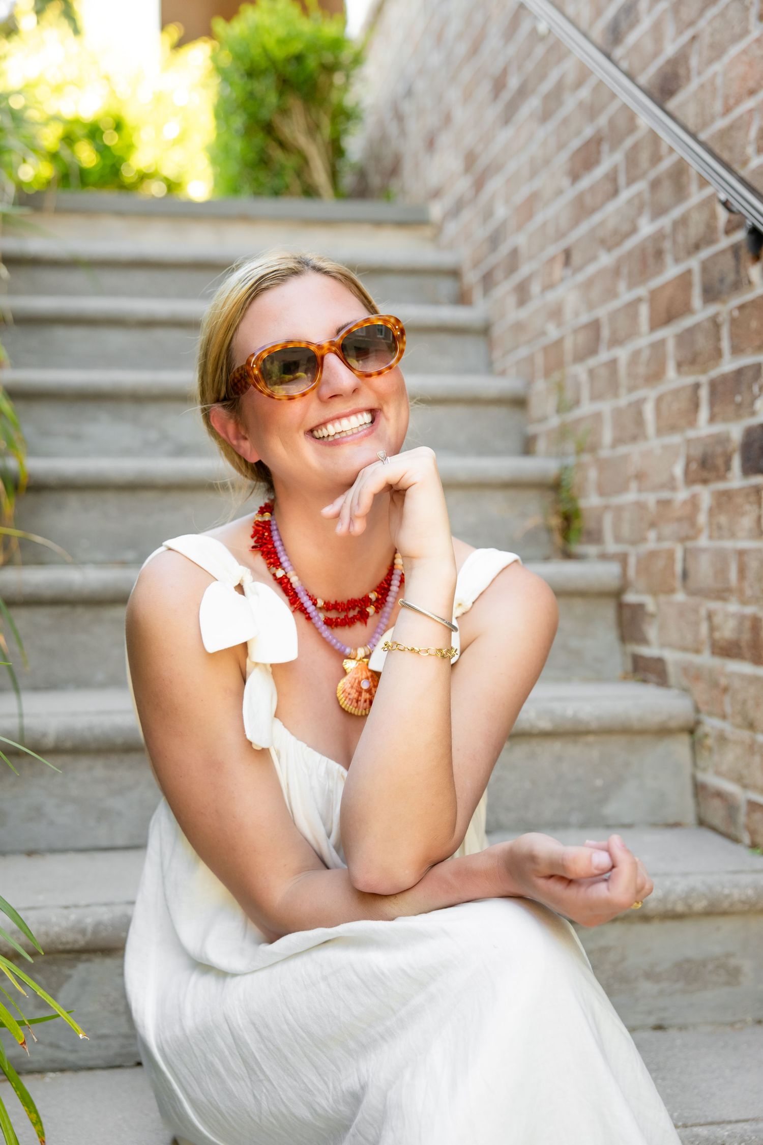Candid outdoor portrait showing white sundress and red beaded necklace on brick staircase.