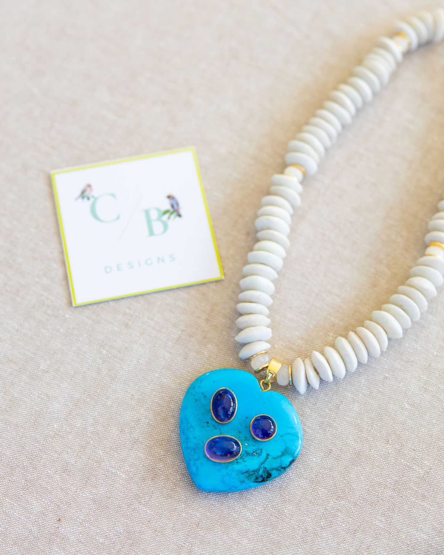 White beaded necklace with bright blue heart-shaped pendant on neutral background.