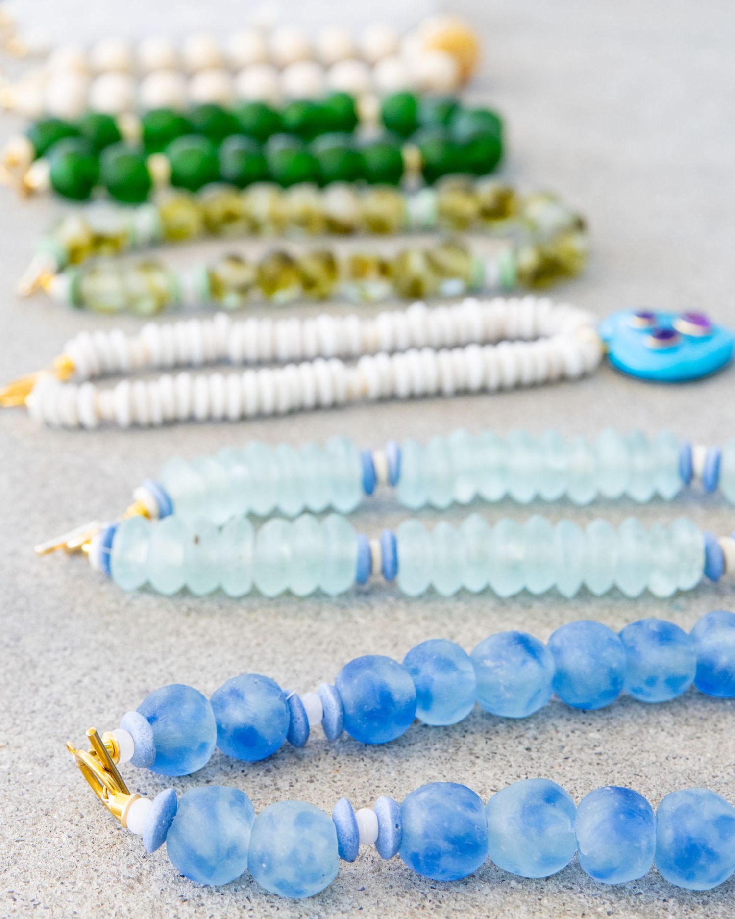 Gradient display of blue glass beaded necklaces arranged in ombre pattern from light to dark blue.